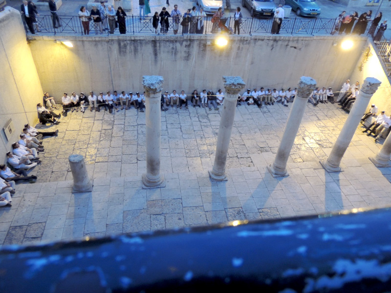 people in black and white clothes sitting on a stone floor with five stone pillars in the middle